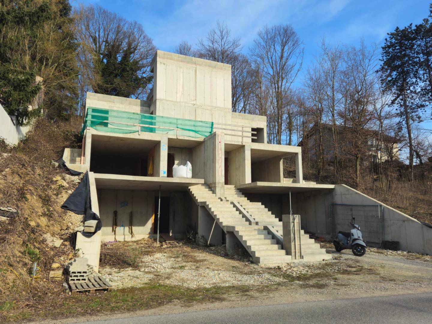 Rohbau der modernen Villa mit sichtbarer Betonkonstruktion und Treppen, umgeben von kahlen Bäumen.