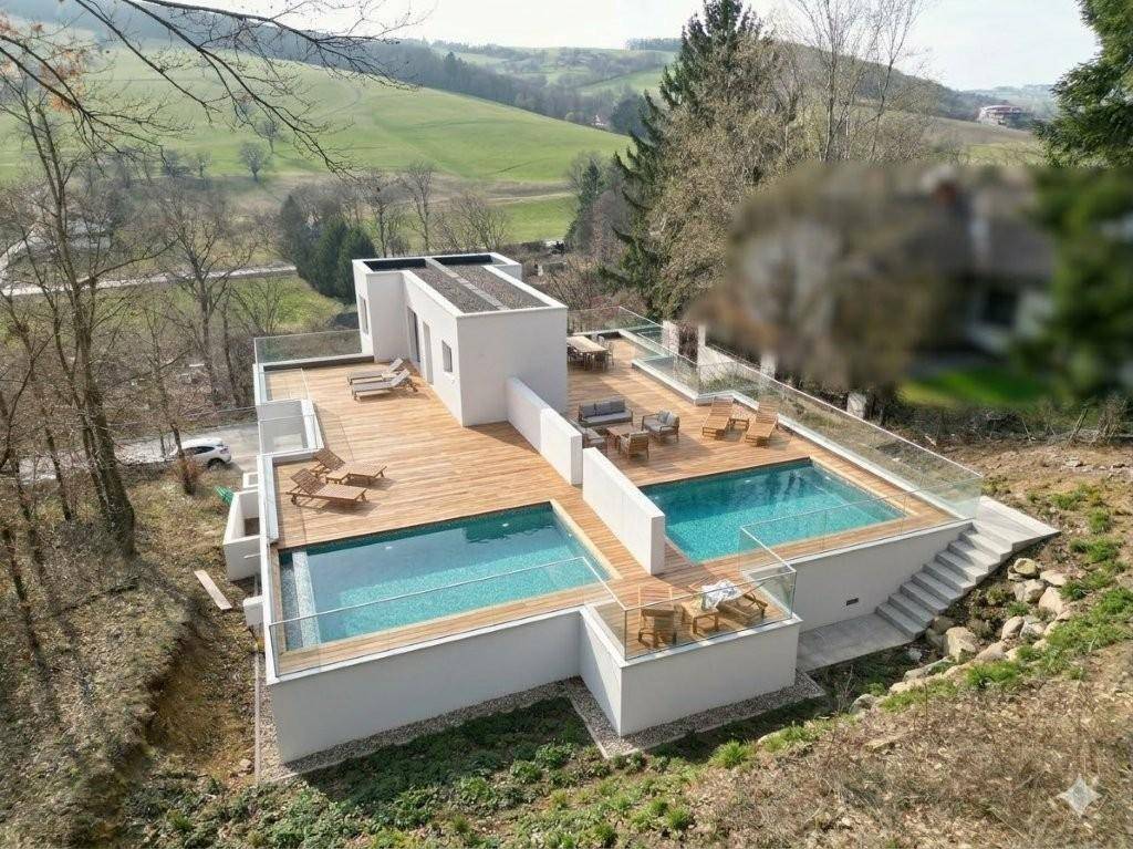 Luxuriöse Außenanlage mit zwei Pools, Holzterrassen und Sitzbereichen, umgeben von grüner Natur.