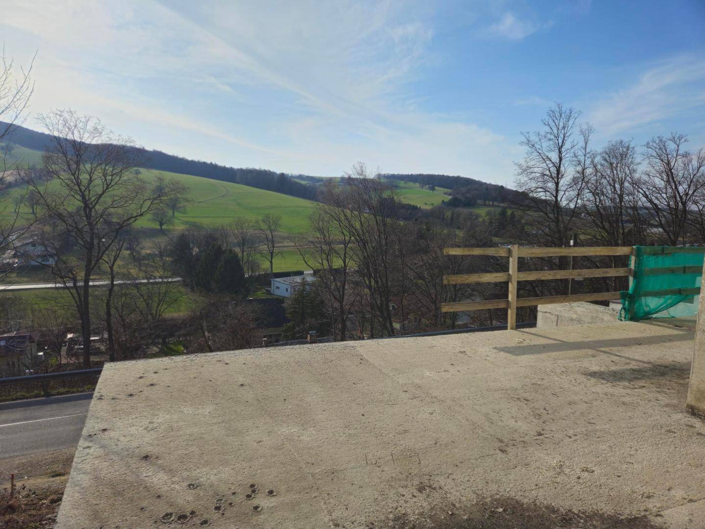 Unfertige Terrasse mit provisorischem Holzgeländer und weitem Blick auf die grüne Landschaft.