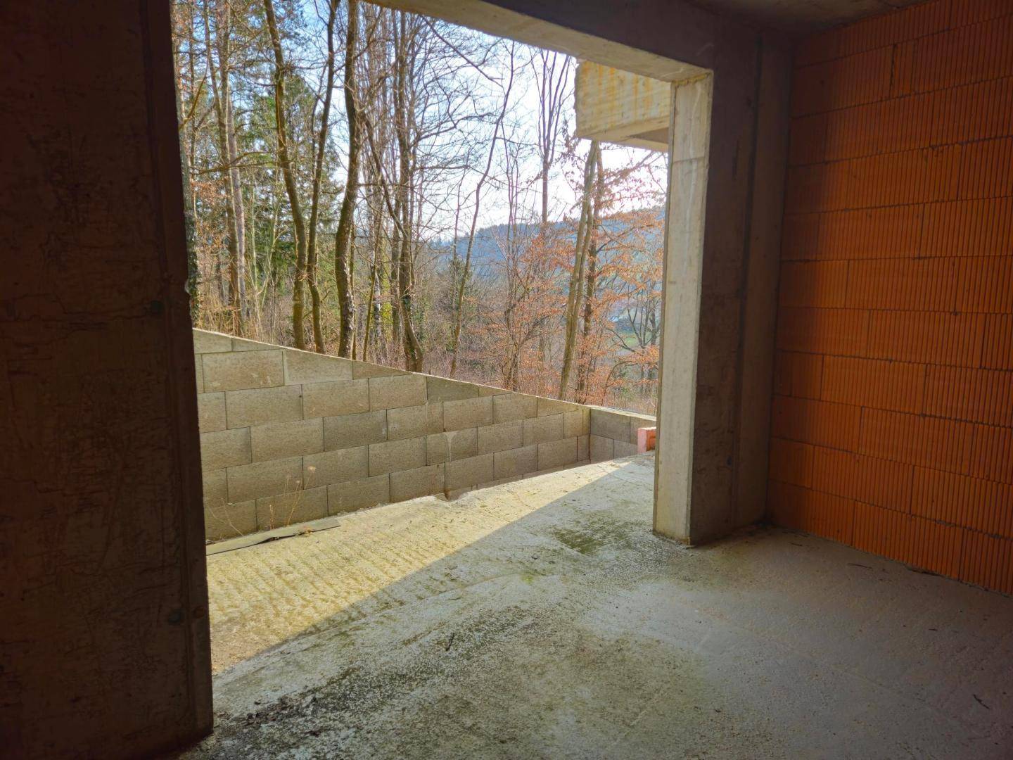 Innenansicht des Rohbaus mit Ziegelwänden und Blick auf eine Betonstützmauer im Außenbereich.