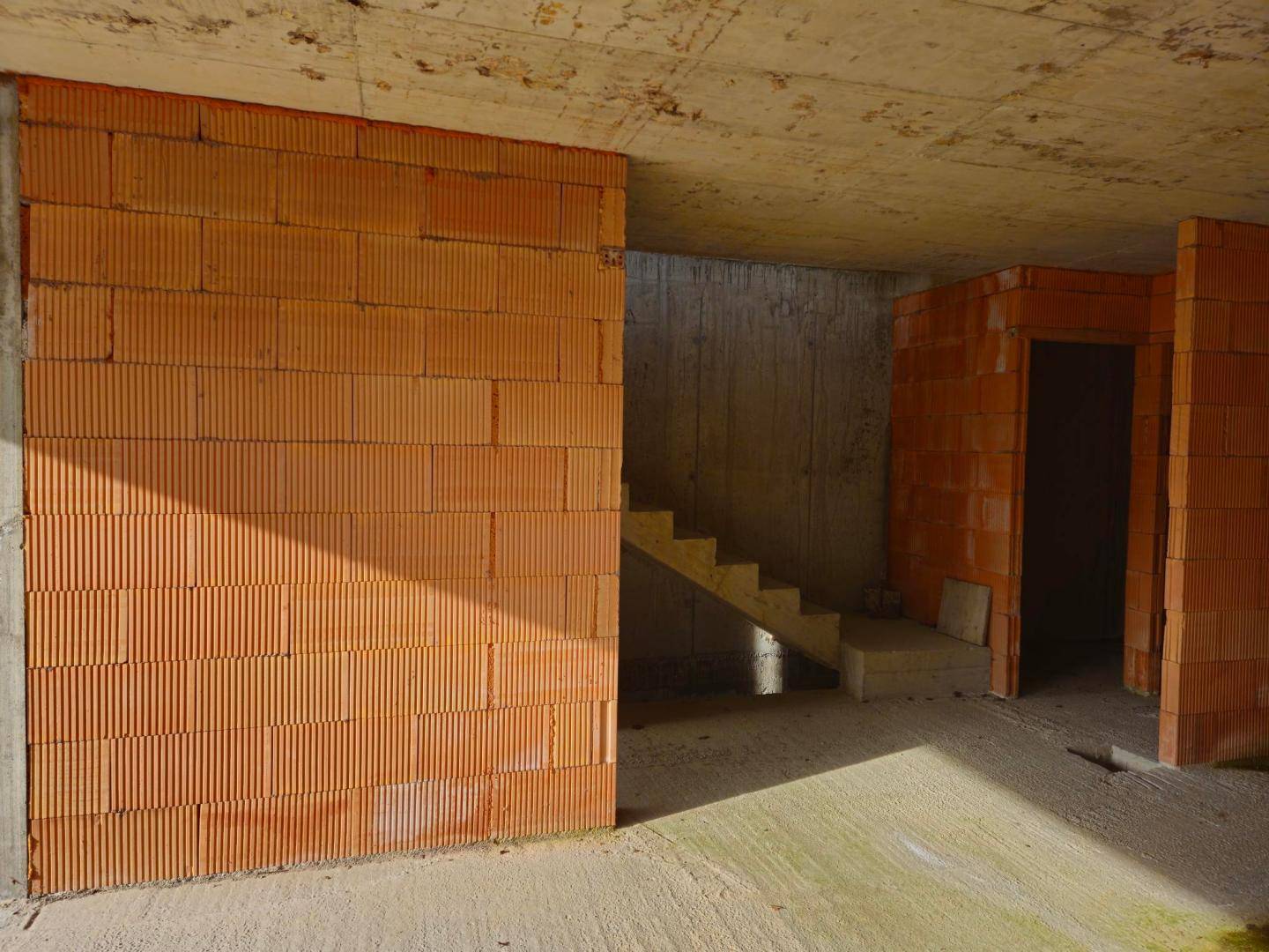 Innenansicht des Rohbaus mit unverputzten Ziegelwänden und einer Betontreppe im Bau.