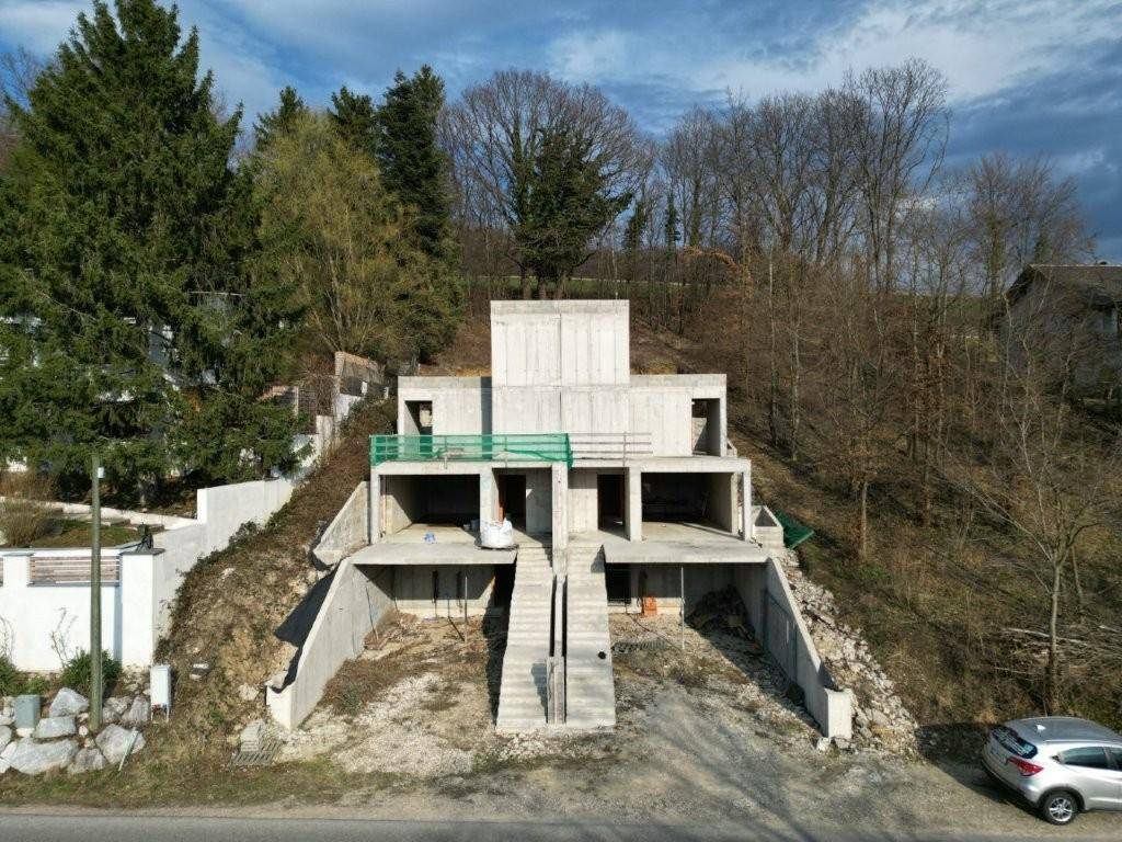 Luftaufnahme des Rohbaus der modernen Villa mit Betonstruktur, umgeben von Bäumen und einer Straße.