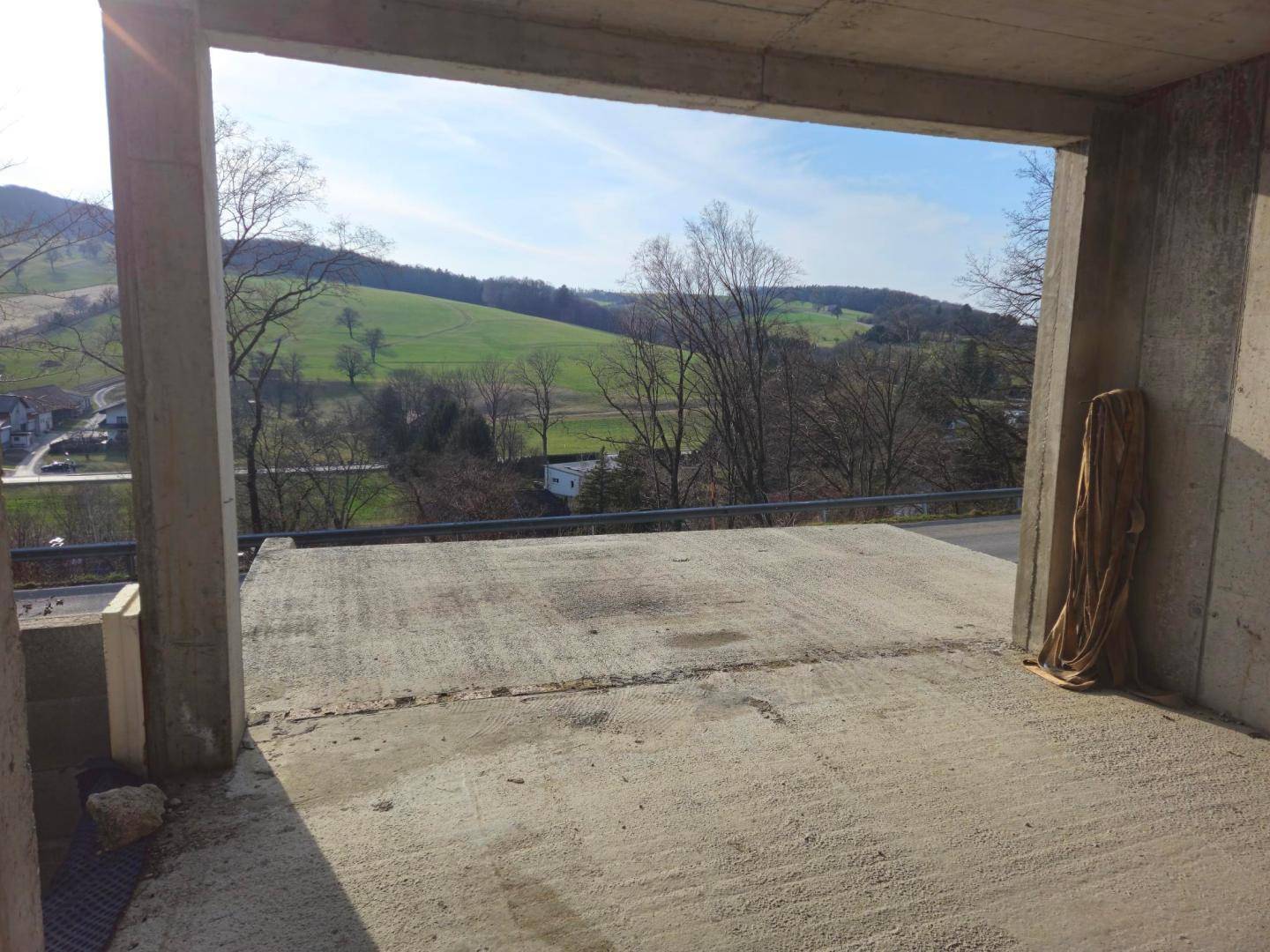 Blick aus einer Rohbauöffnung auf die weite grüne Hügellandschaft unter blauem Himmel.