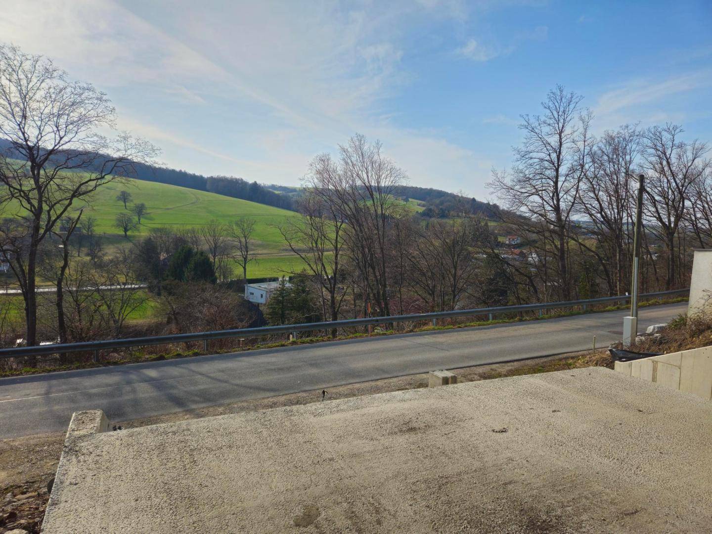 Weitläufiger Blick über eine Straße und grüne Hügellandschaft von der Baustelle aus.