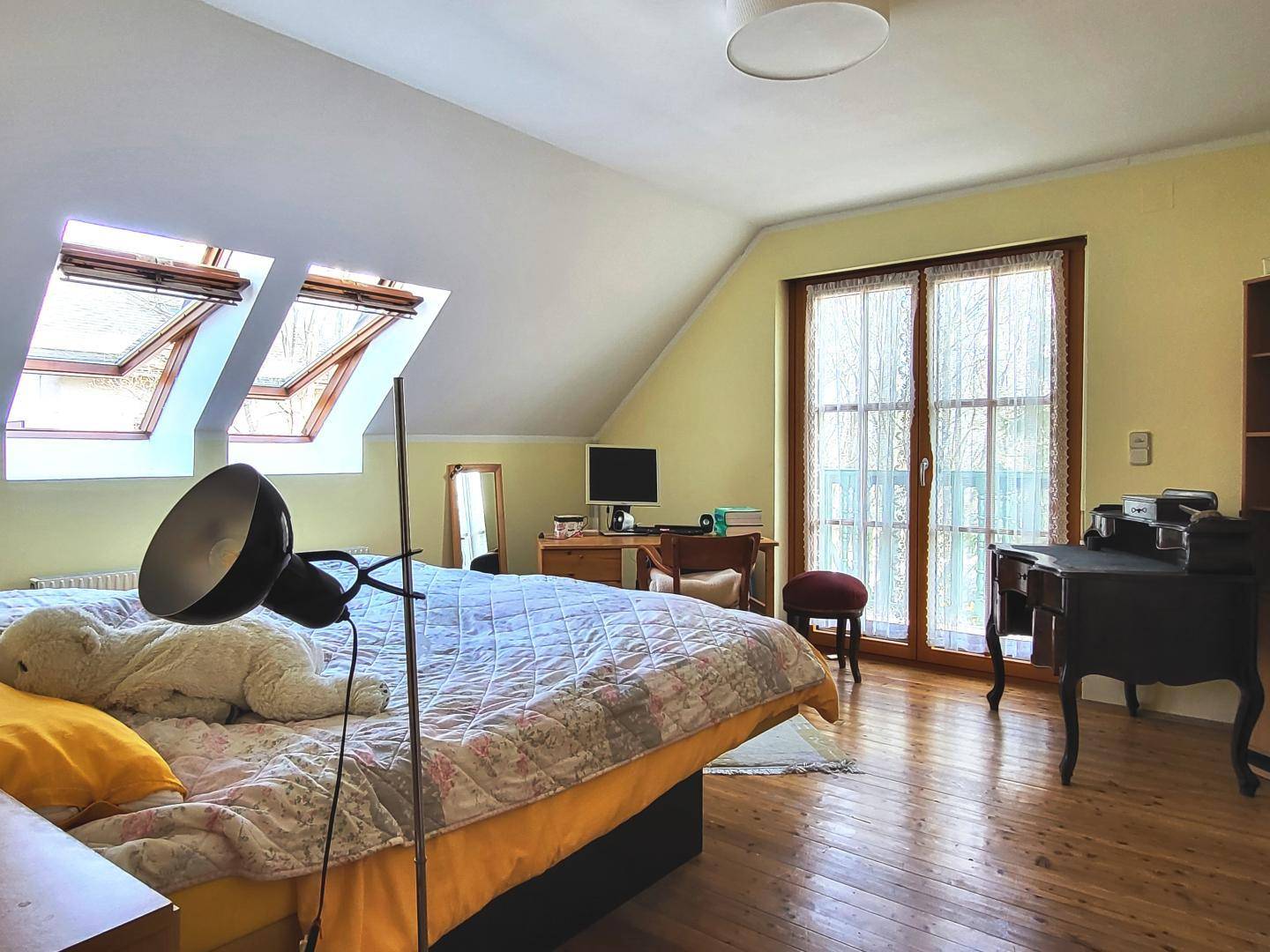 Gemütliches Schlafzimmer im Dachgeschoss mit Holzboden, Bett, Schreibtisch und zwei Dachfenstern.
