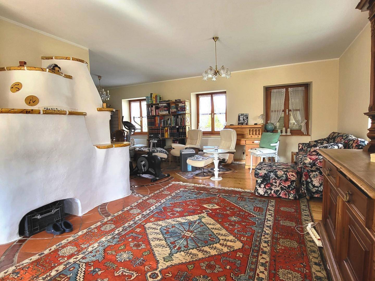 Helles Wohnzimmer mit traditionellem Kachelofen, Sofa und Bücherregalen.