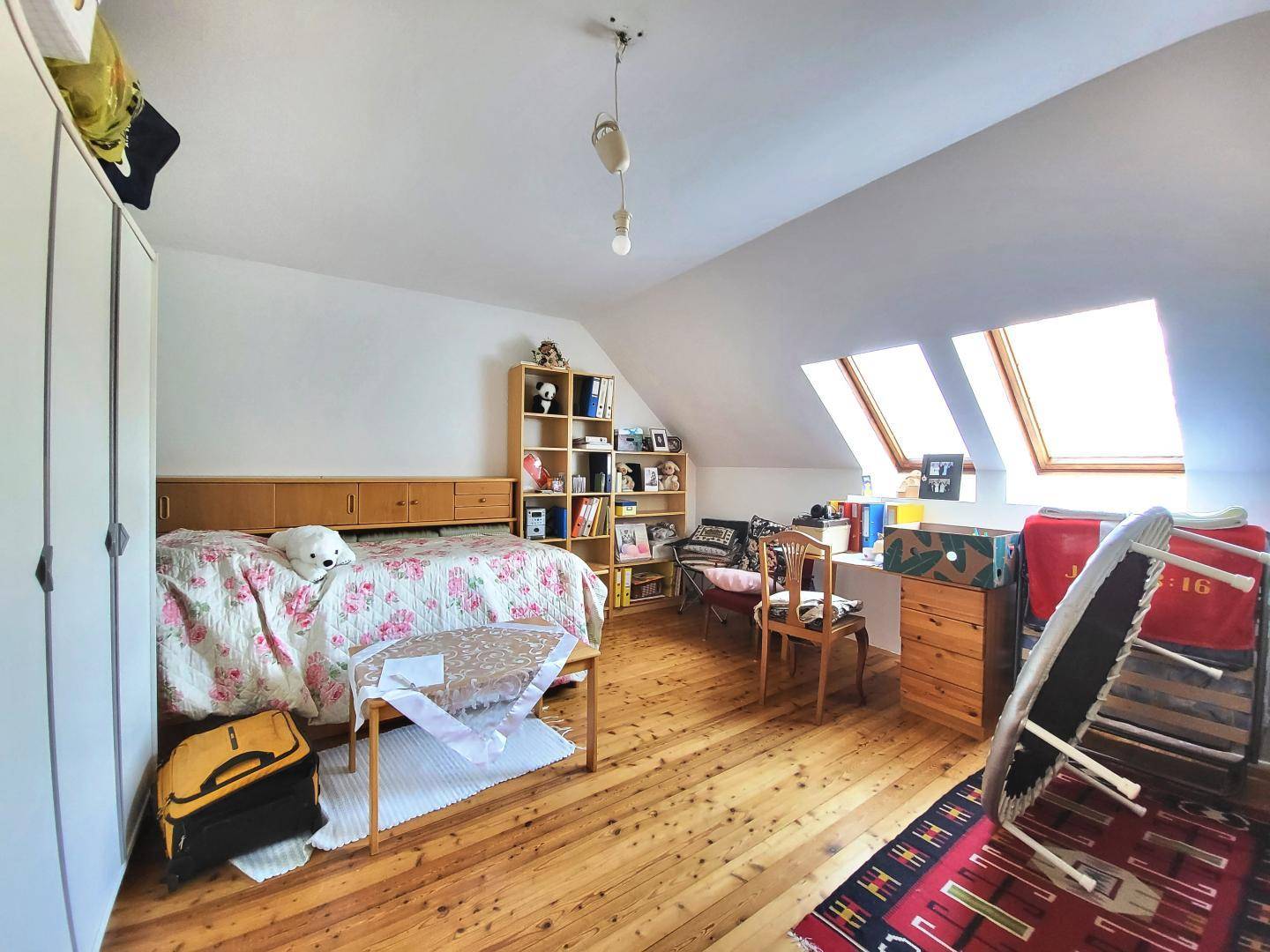 Weiteres Schlafzimmer im Dachgeschoss mit Holzboden, Schrank und zwei hellen Dachfenstern.