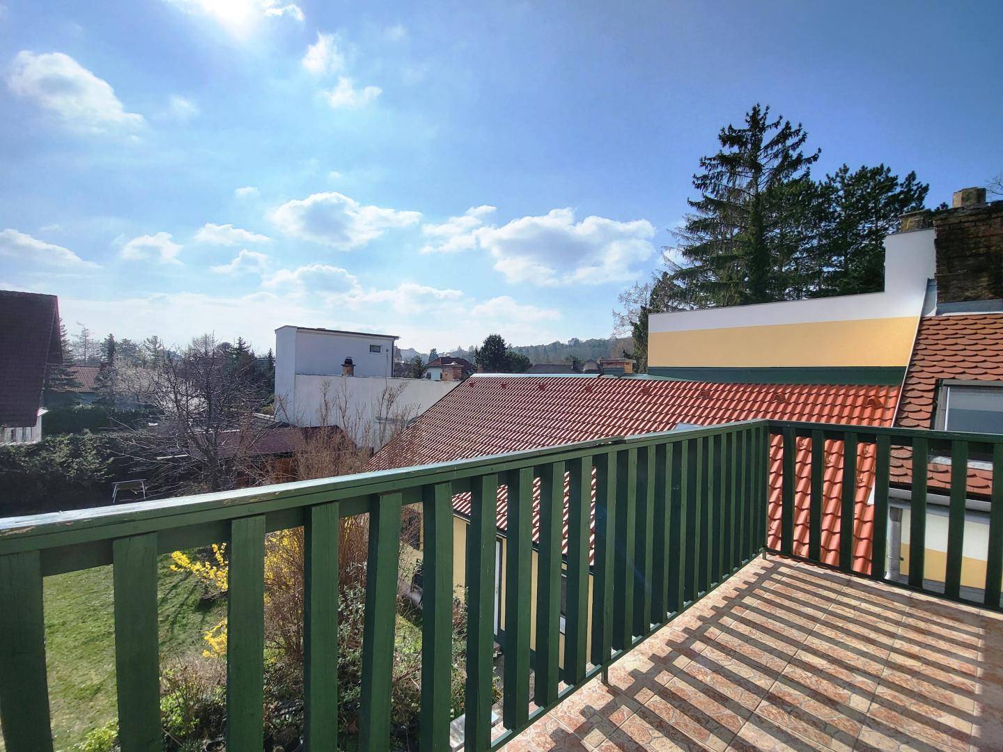 Ausblick vom Balkon mit grüner Brüstung auf die umliegenden Dächer und den Garten.