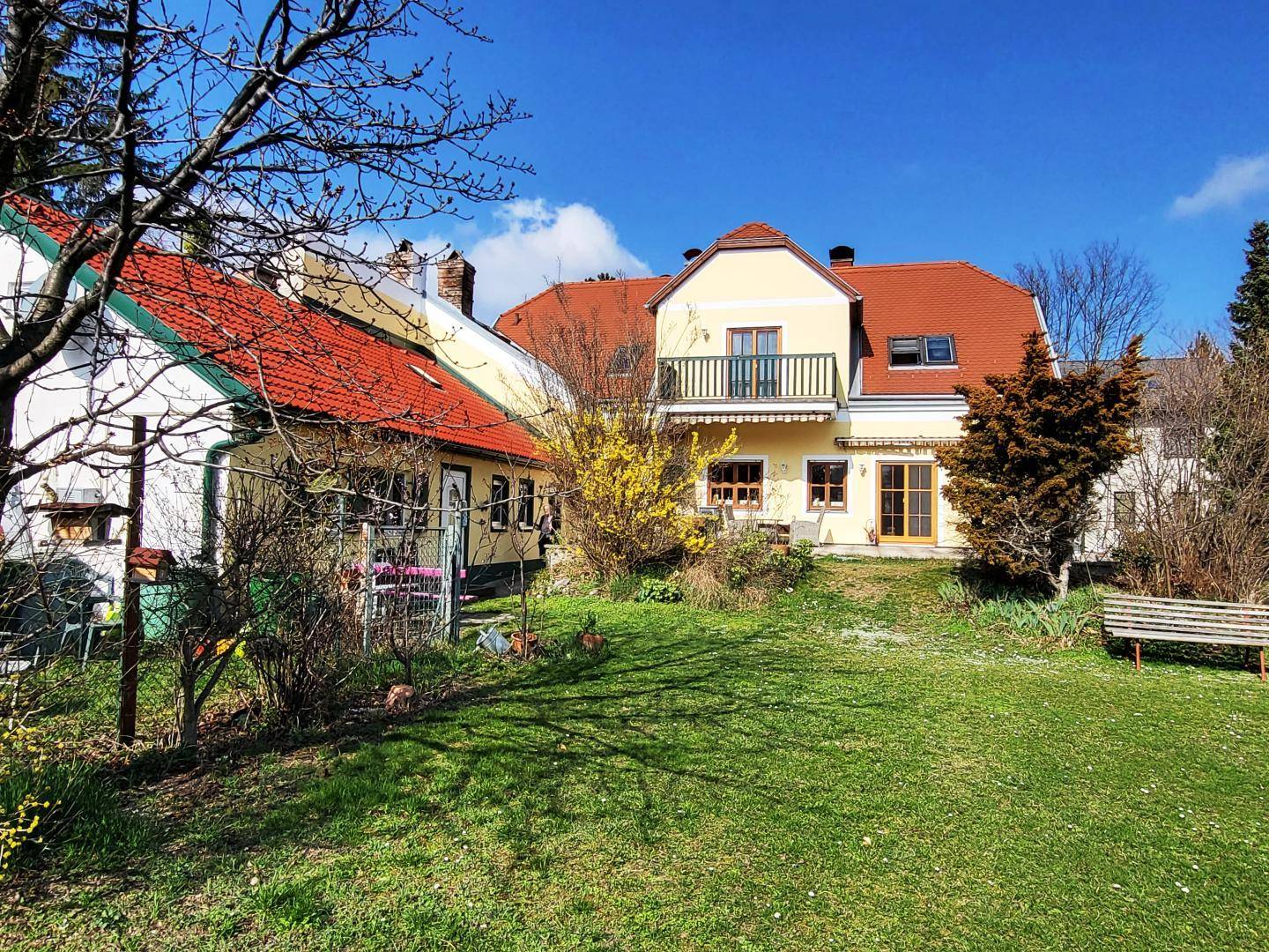 Weitläufiger Gartenbereich mit Rasenfläche und Blick auf das gelbe Wohnhaus mit Balkon.