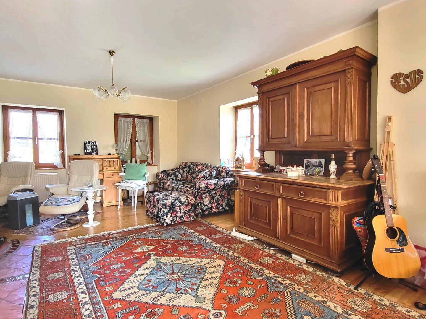Wohnzimmer mit großem Holzschrank, floral gemustertem Sofa und mehreren Fenstern.