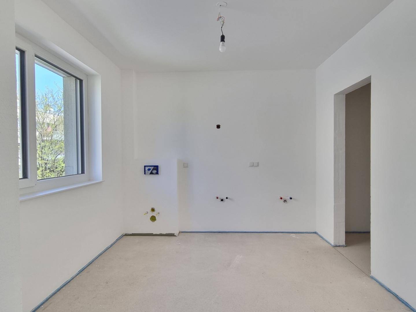 Unfertiges Badezimmer mit Fenster und vorbereiteten Anschlüssen für Sanitärinstallationen.