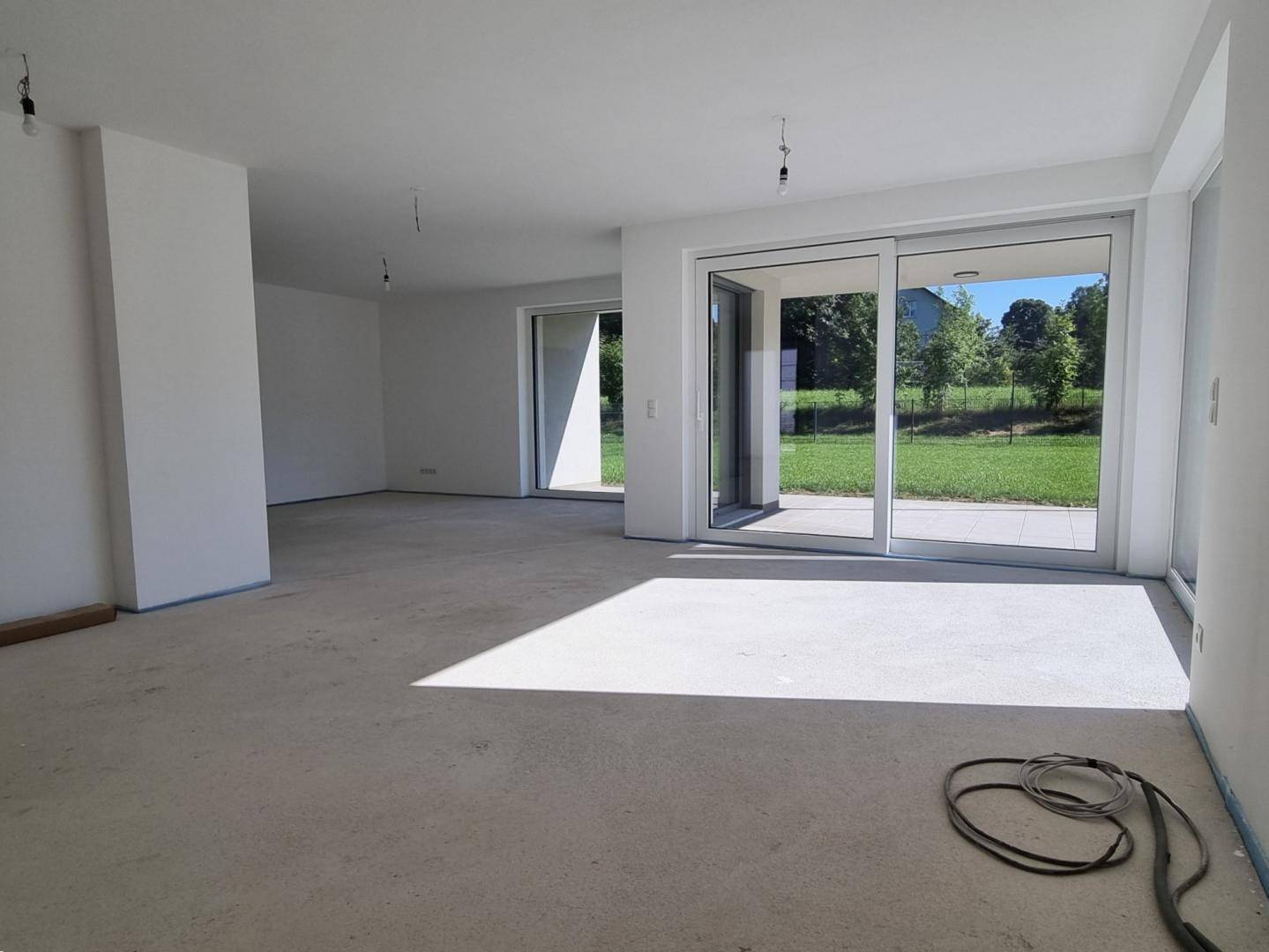 Geräumiger, unfertiger Wohnbereich mit viel Tageslicht und Blick ins Grüne.