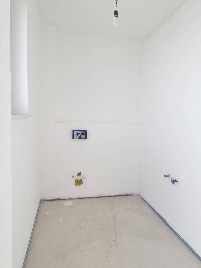 Kleiner Raum im Rohbau mit Anschlüssen für ein WC und Fenster, ideal als Gäste-WC.