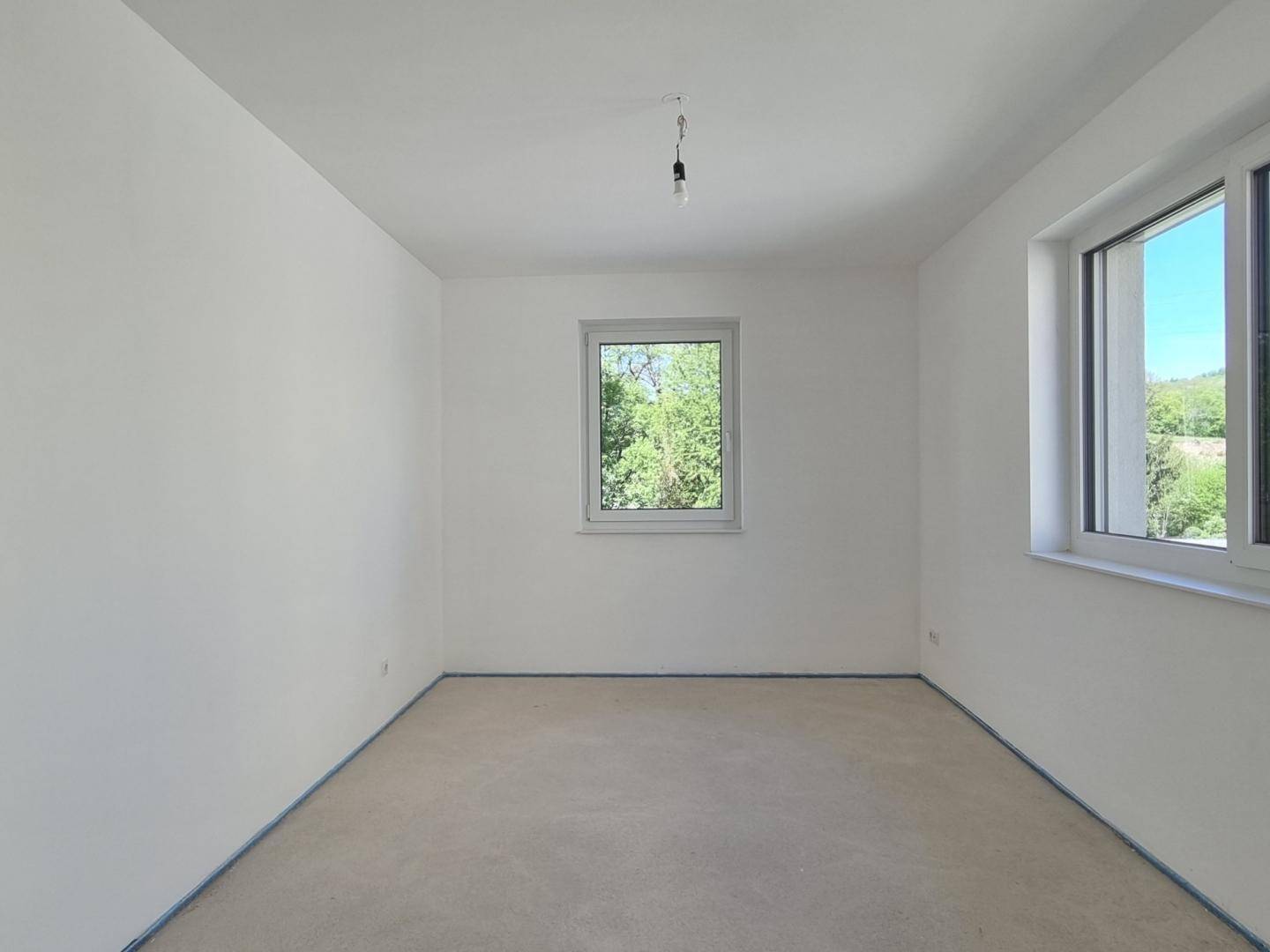 Heller Raum im Rohbau mit zwei Fenstern und Blick ins Grüne, ideal als Schlafzimmer.