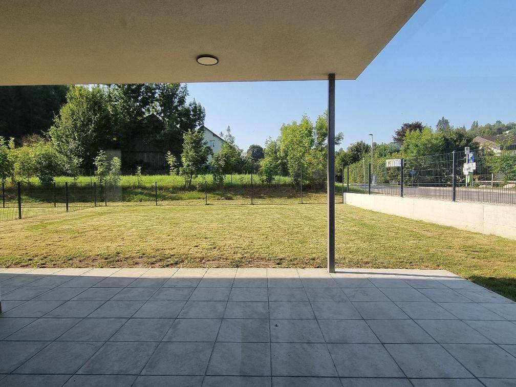 Überdachte Terrasse mit Fliesenboden und Blick auf den grünen Gartenbereich des Hauses.