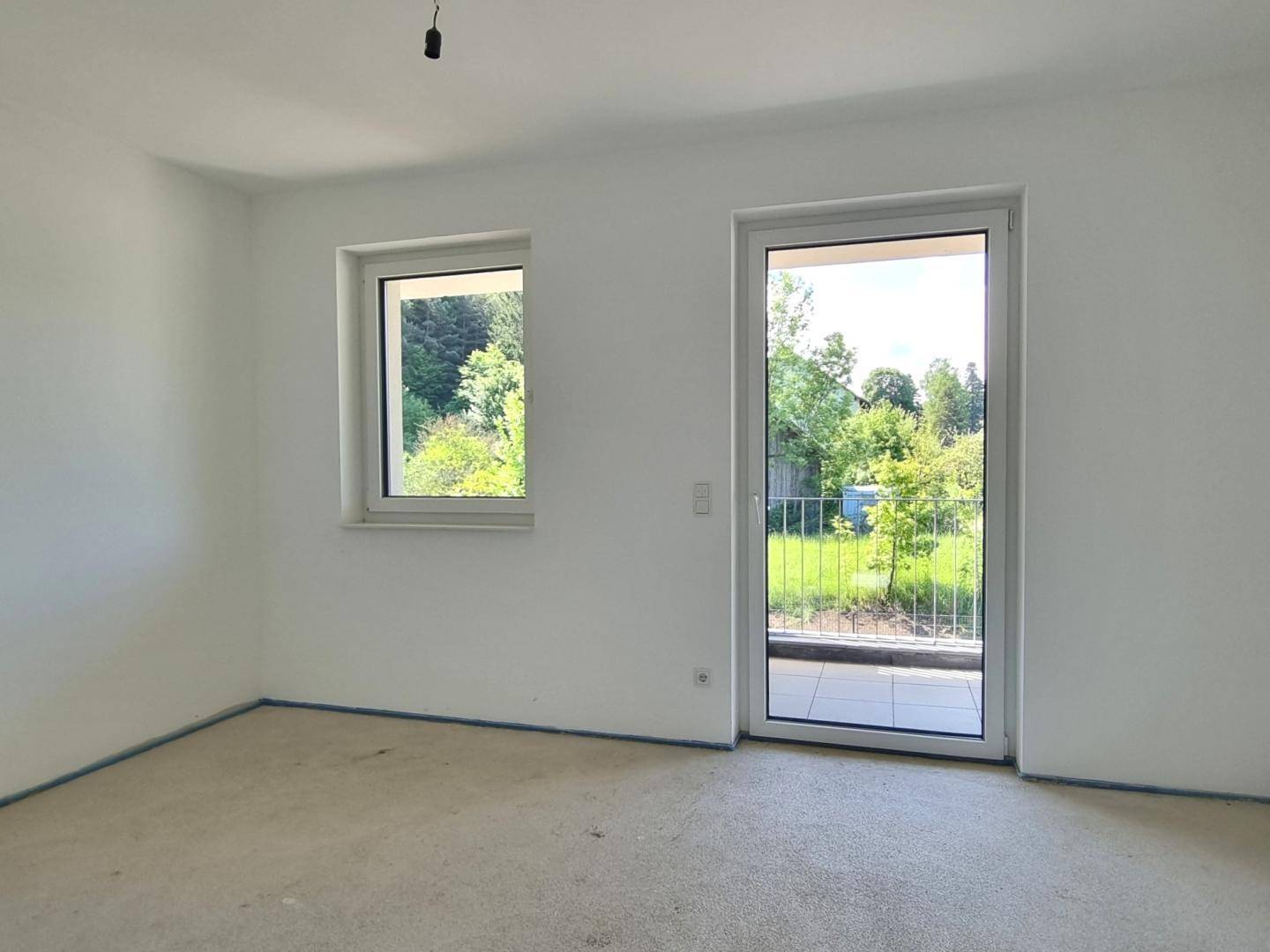 Helles Schlafzimmer im Rohbau mit Fenster und Zugang zum Balkon.