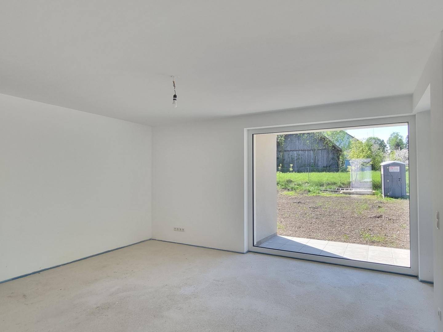 Heller Raum im Rohbau mit großem Fenster und Blick auf den zukünftigen Gartenbereich.