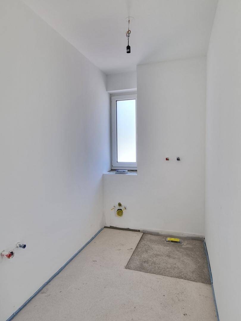 Unfertiges Badezimmer mit Fenster und Anschlüssen für Sanitäranlagen, bereit für den Ausbau.