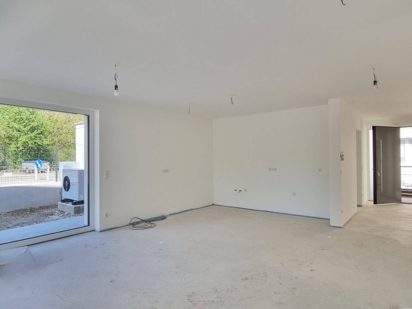 Unfertiger Wohnbereich mit Eingangstür und großem Fenster zum Außenbereich, bereit für den Ausbau.