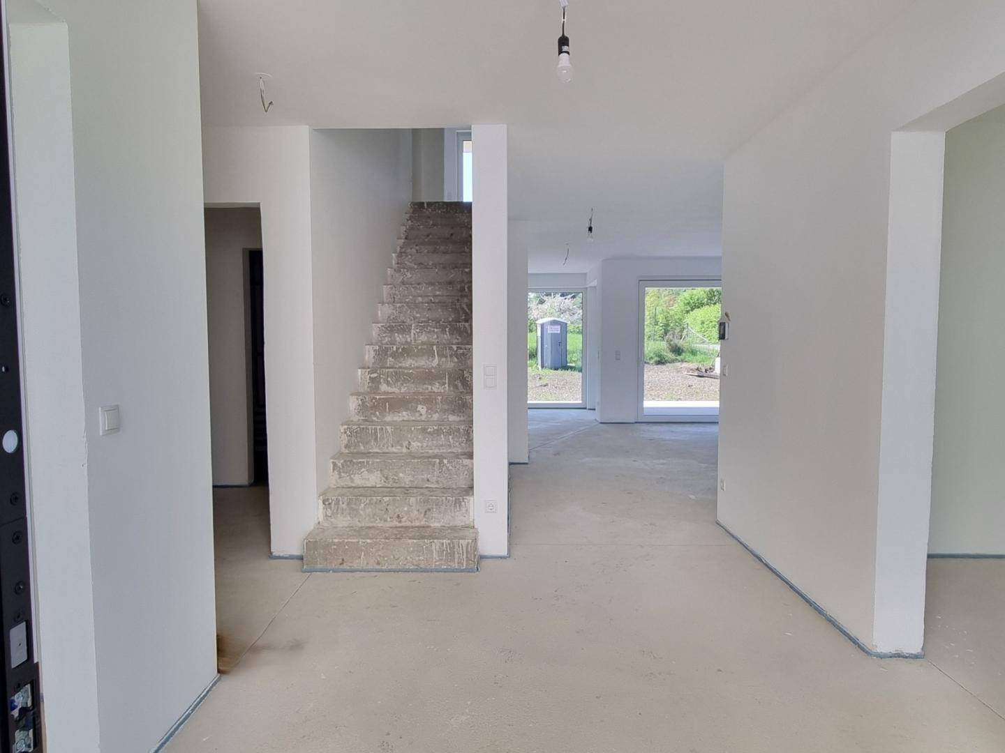Eingangsbereich im Rohbau mit Treppe und offenem Blick in die zukünftigen Wohnbereiche.