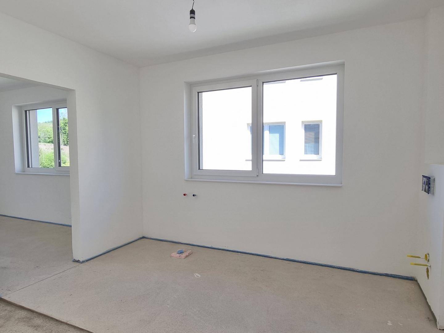 Heller Raum im Rohbau mit Fenster und Blick auf ein gegenüberliegendes Gebäude.