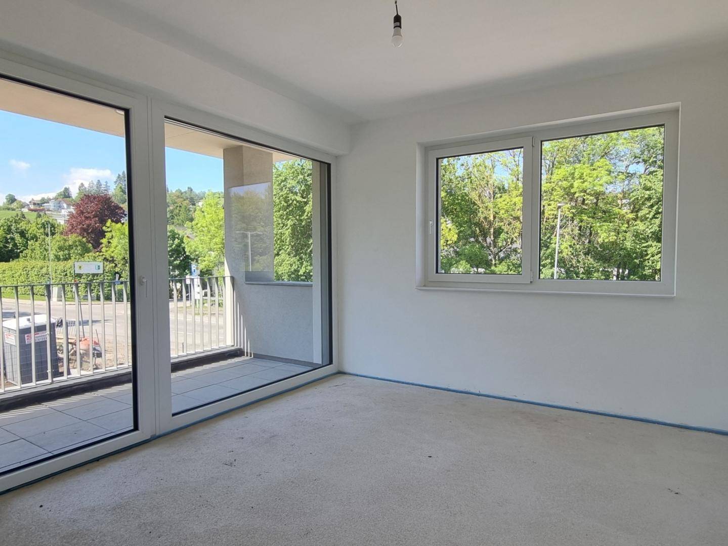 Helles Schlafzimmer im Rohbau mit Zugang zum Balkon und Blick ins Grüne.