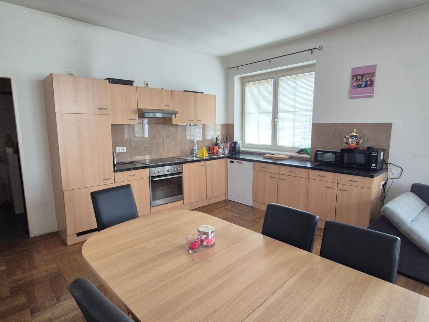 Funktionale Küche mit hellen Holzschränken, Essbereich und Fenster.