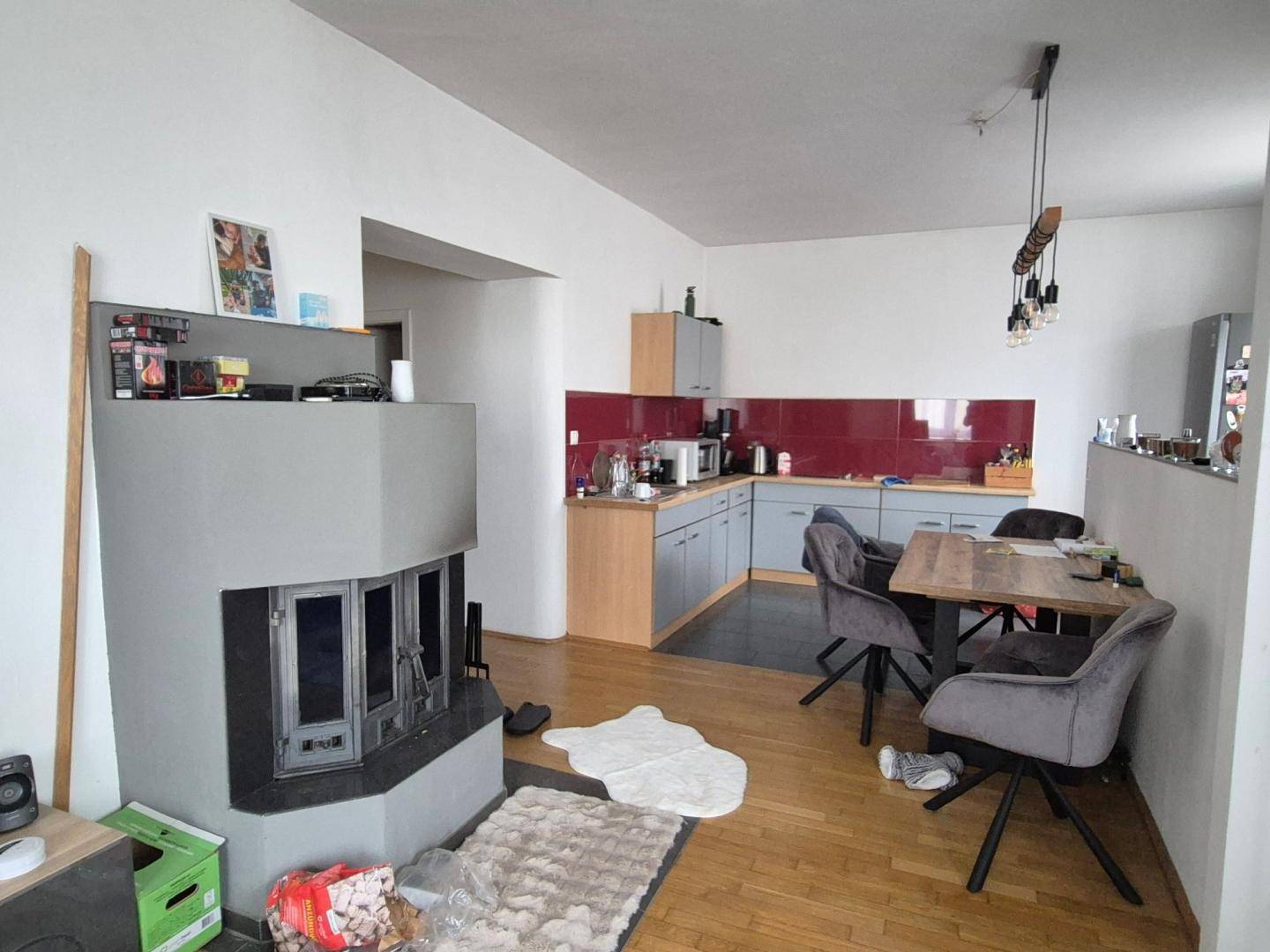 Offener Wohnbereich mit Kamin, Essplatz und angrenzender Küche mit roten Akzenten.