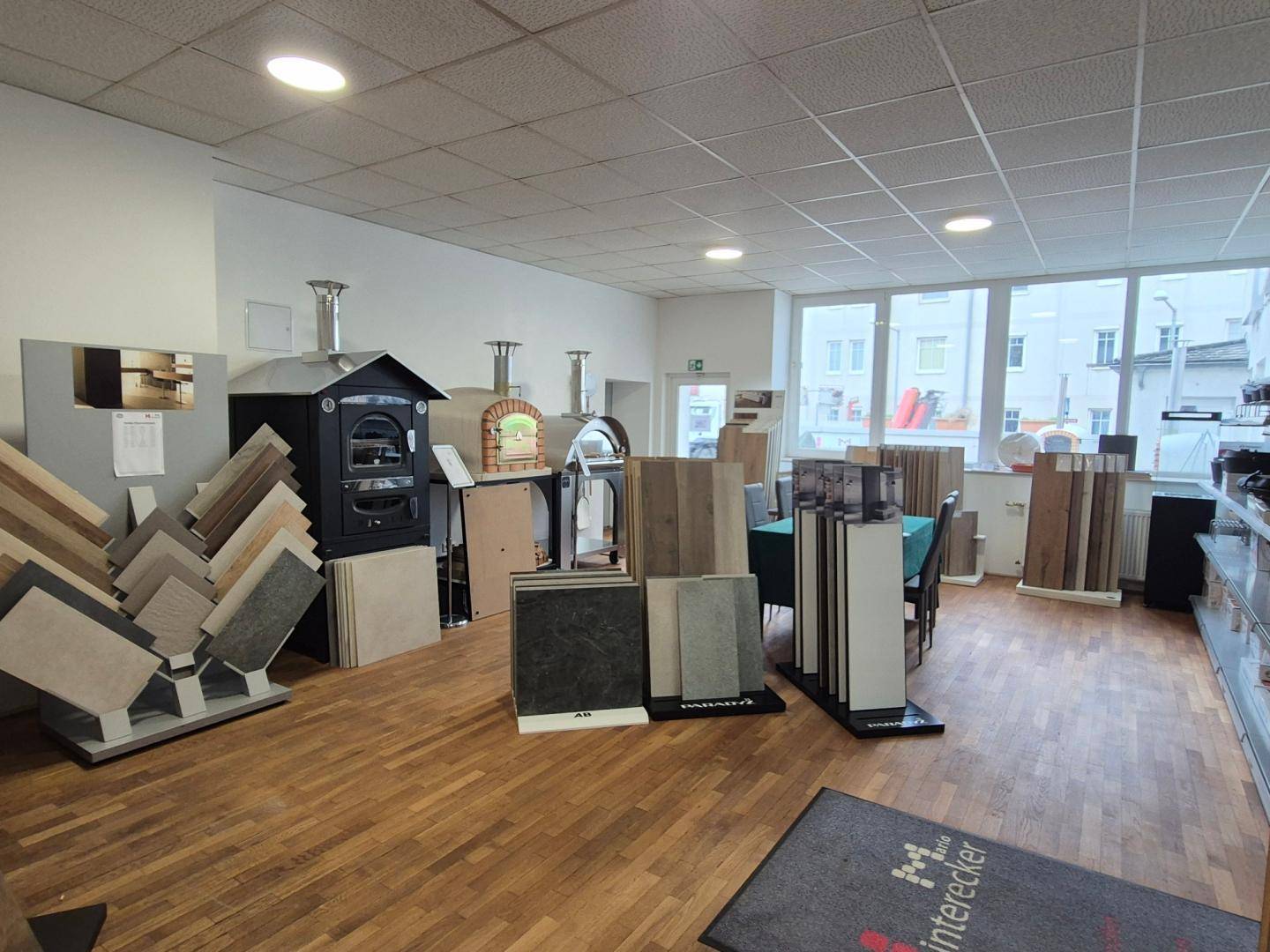 Geräumiger Ausstellungsraum mit verschiedenen Bodenbelägen und Outdoor-Öfen.