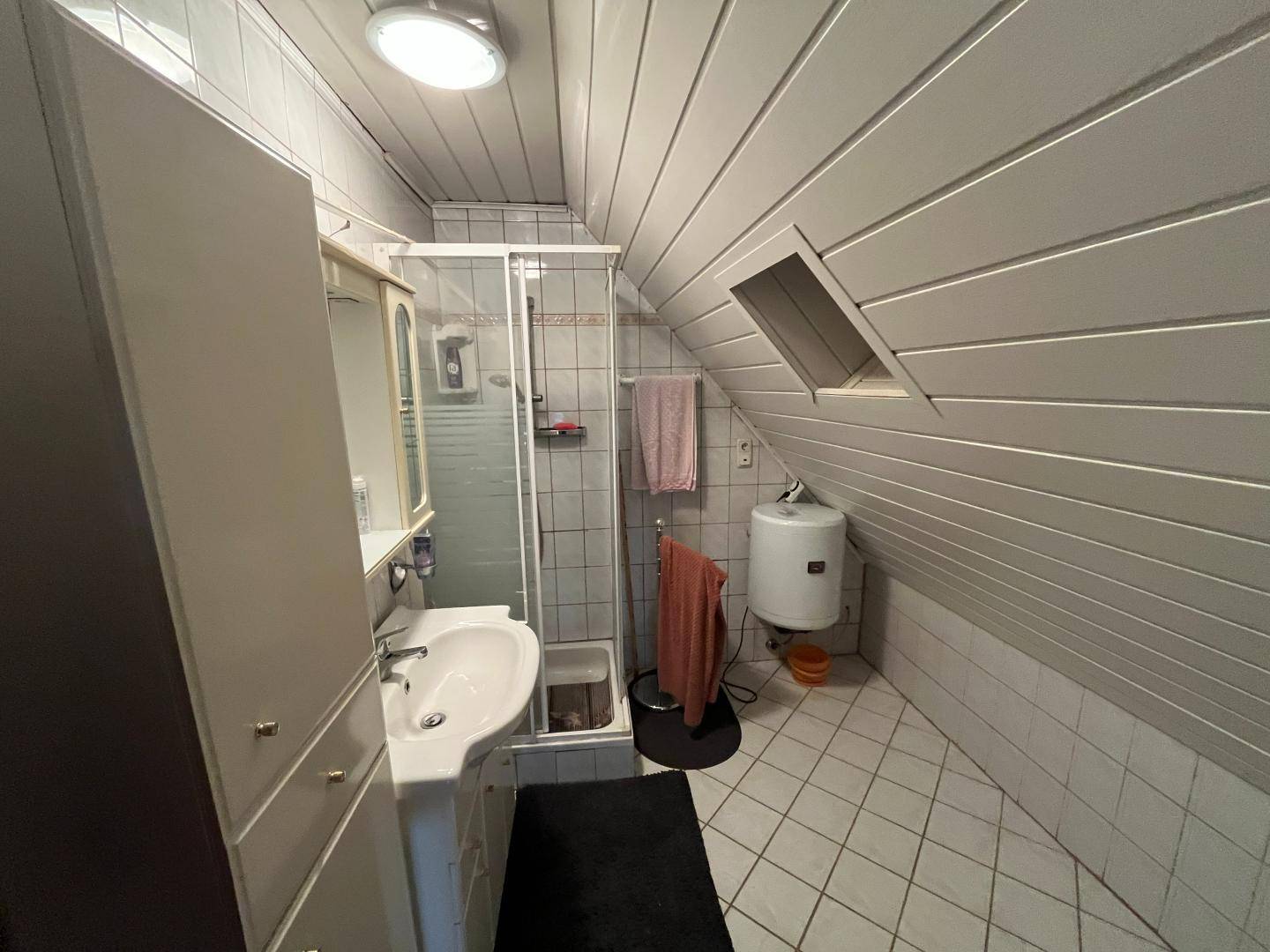 Dachgeschoss-Badezimmer mit Schrägdach, Dusche und weißen Fliesen.