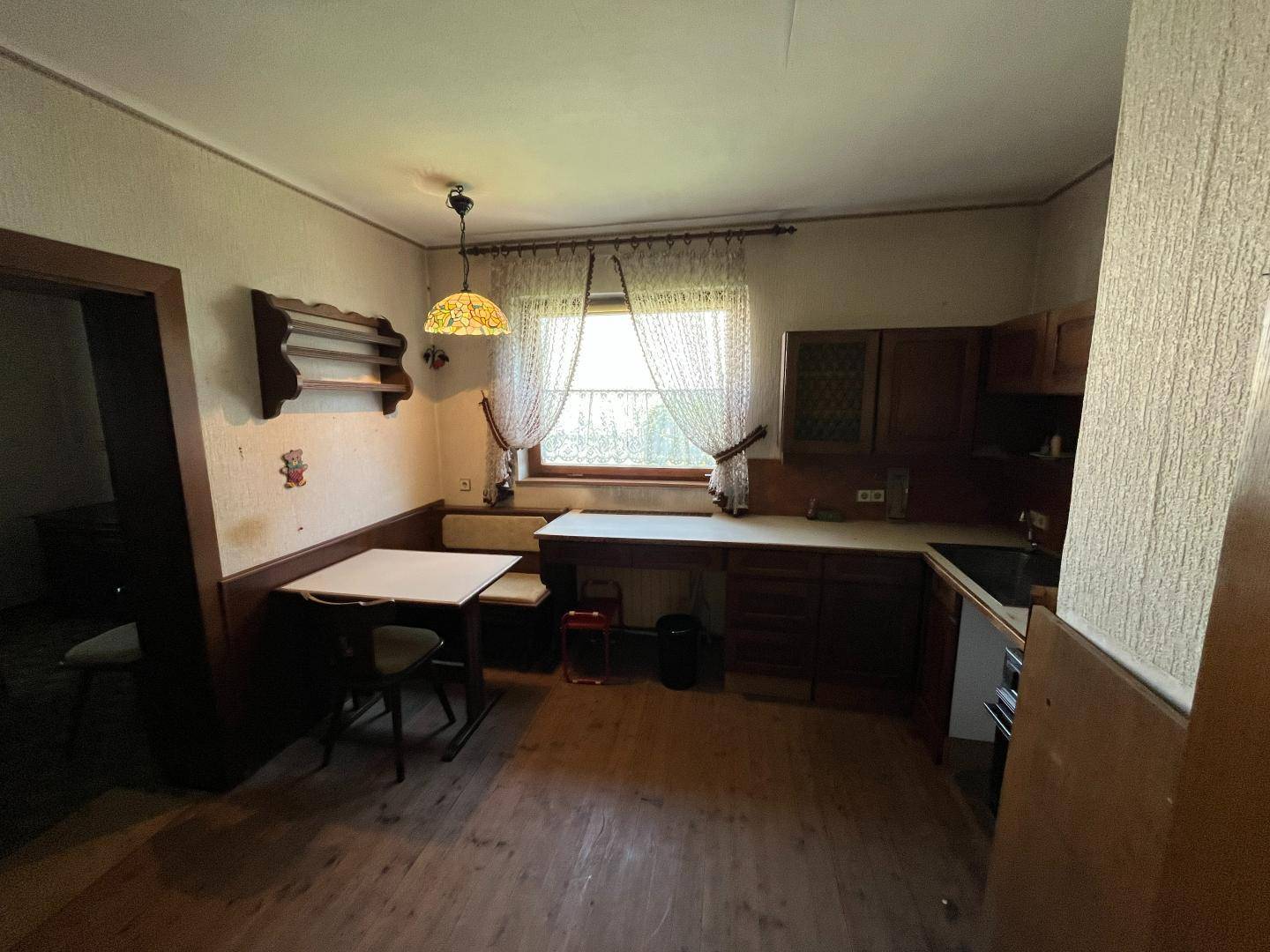 Rustikale Küche mit Holzboden, dunklen Holzschränken und einem kleinen Essbereich am Fenster.