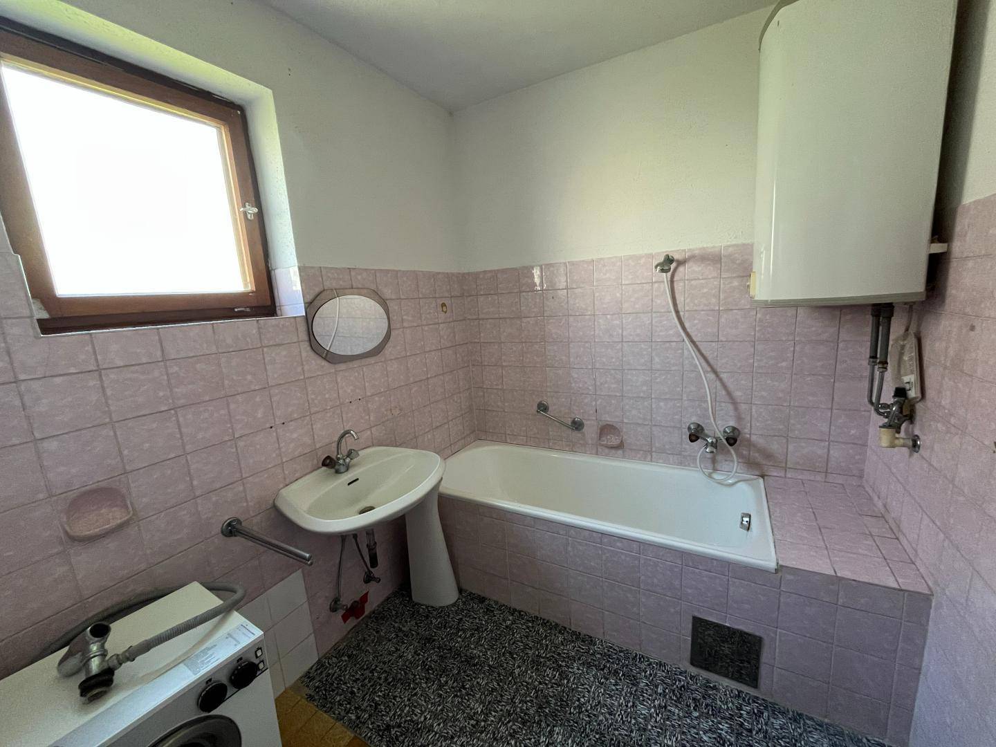 Badezimmer im Stil der 80er Jahre mit rosa Fliesen, Badewanne und Fenster.