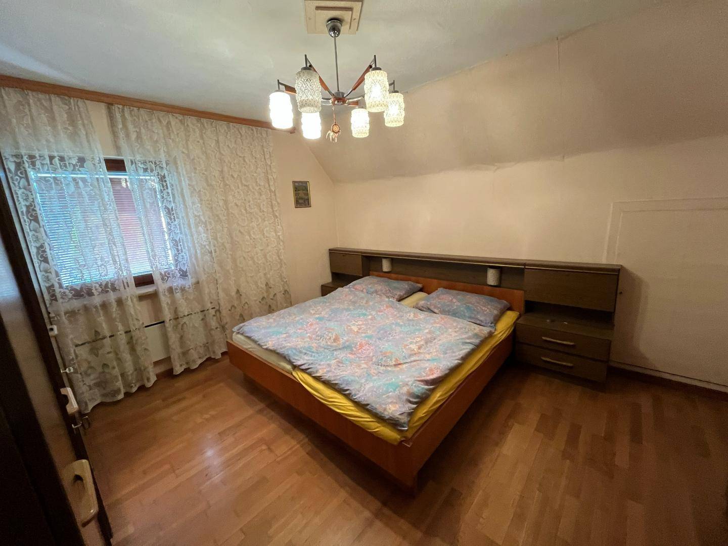 Schlafzimmer mit Holzboden, Doppelbett und einem Fenster mit Jalousien.