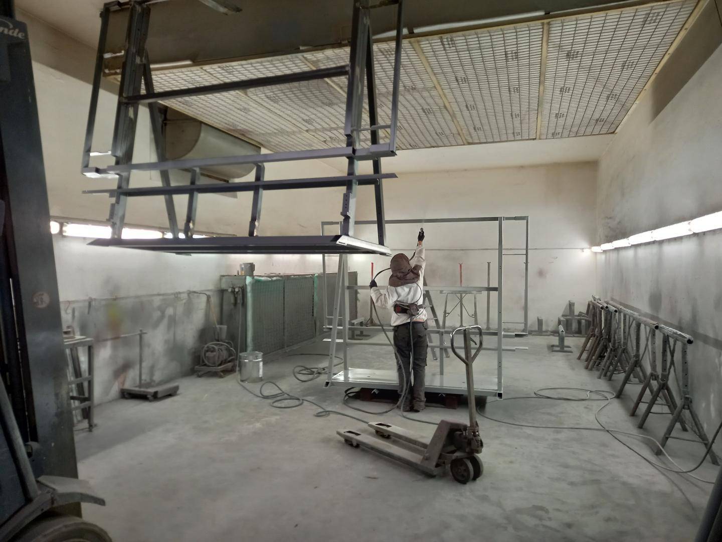 Innenansicht einer Spritzkabine oder Lackiererei, wo ein Arbeiter Metallrahmen besprüht.