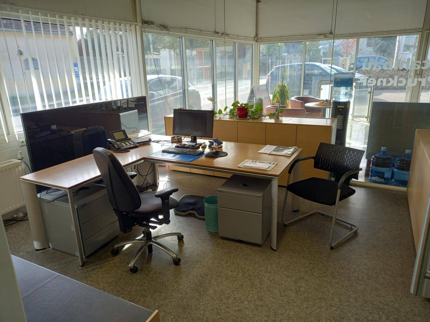 Helles Büro mit großem Eckschreibtisch, Bürostühlen und großen Fenstern, die viel Tageslicht hereinlassen.