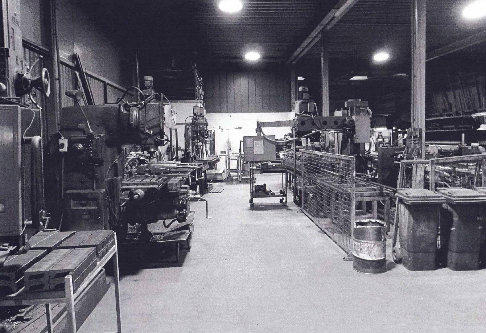 Schwarz-Weiß-Bild einer Werkstatt mit einer Reihe von schweren Industriemaschinen und Werkbänken.