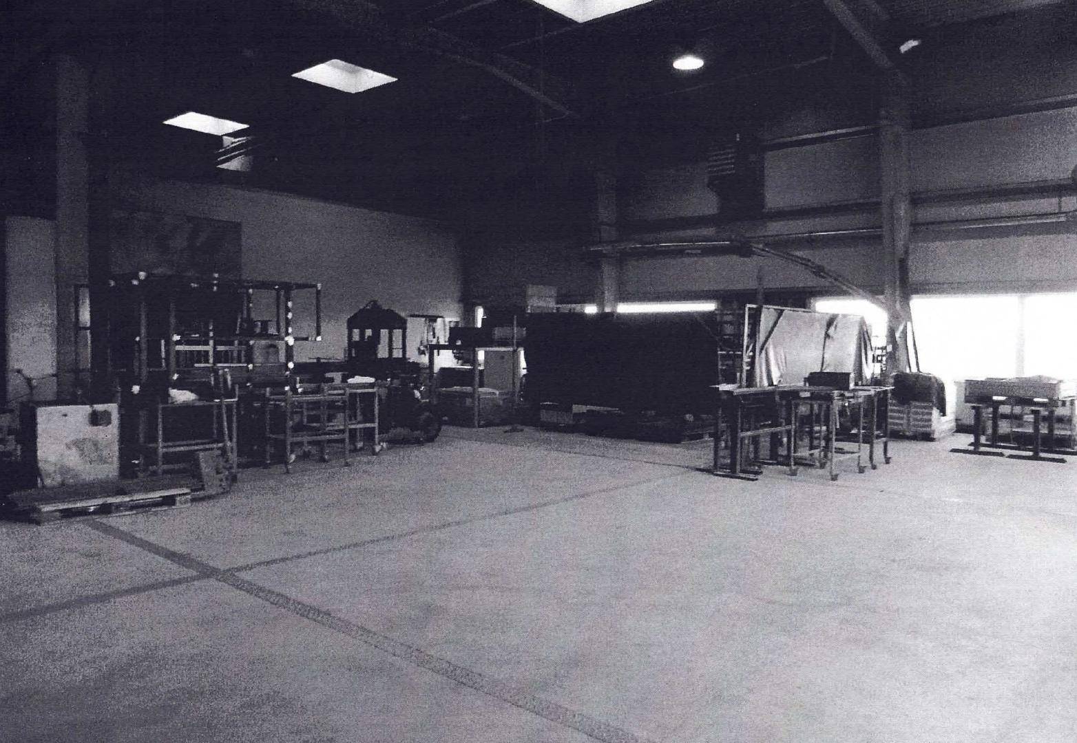 Geräumige, leere Lagerhalle in Schwarz-Weiß mit Betonboden und einigen Geräten, die auf weitere Nutzung warten.