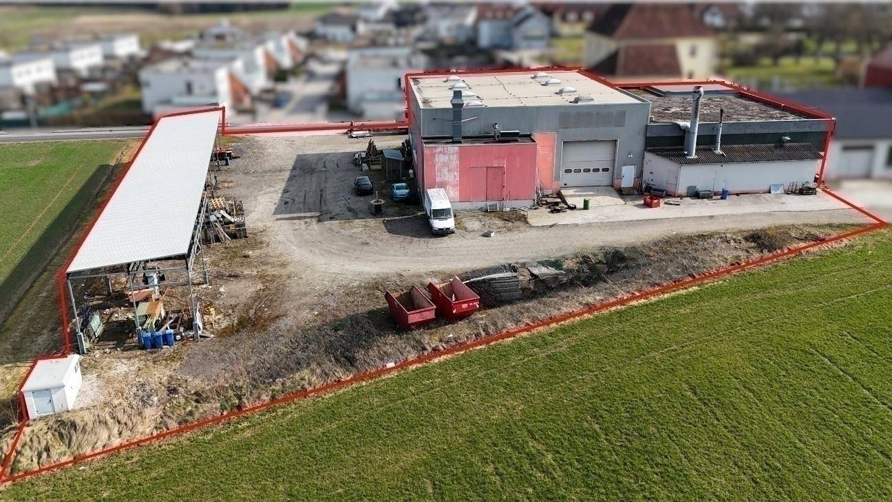 Luftaufnahme eines Gewerbegrundstücks mit rot markierten Grenzen, Gebäuden, Parkflächen und angrenzenden Feldern.