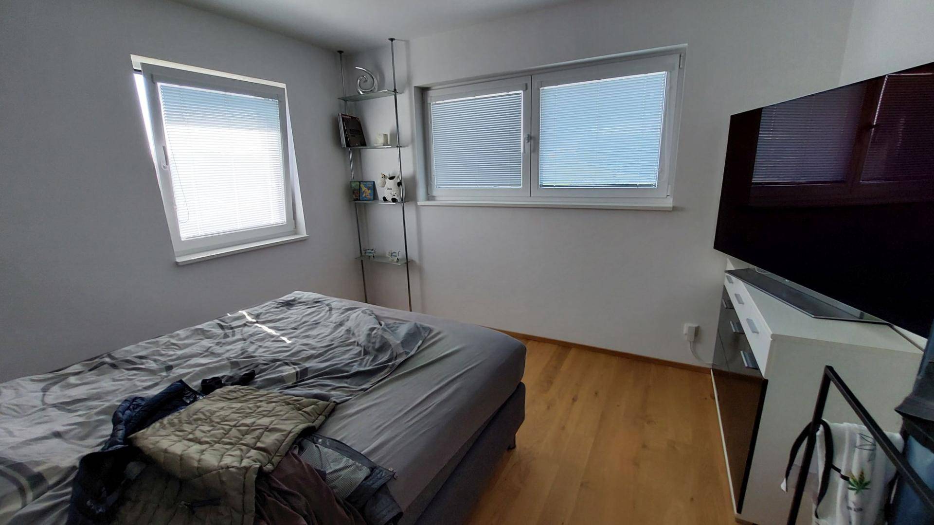 Schlafzimmer mit Holzboden, großem Bett und einem an der Wand montierten Fernseher.