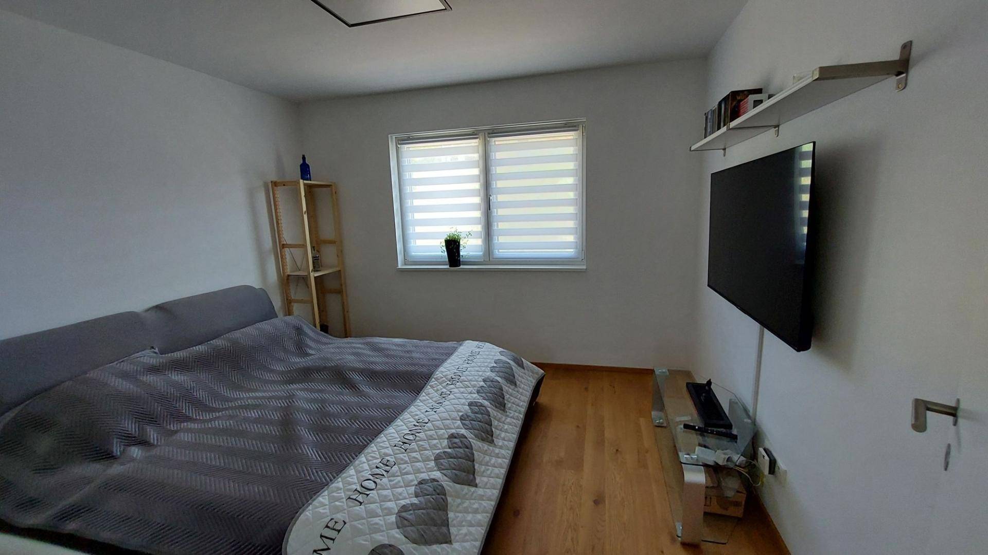 Gemütliches Schlafzimmer mit Holzboden, Doppelbett und einem Wandregal.