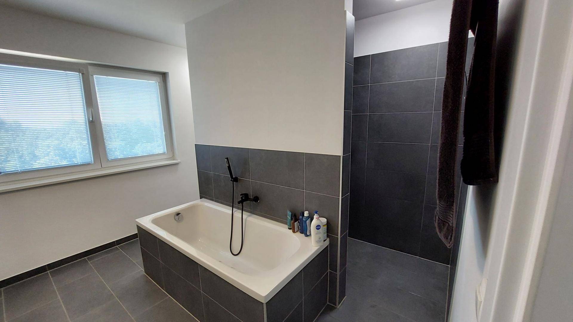 Helles Badezimmer mit Badewanne und geräumiger begehbarer Dusche in modernem Design.