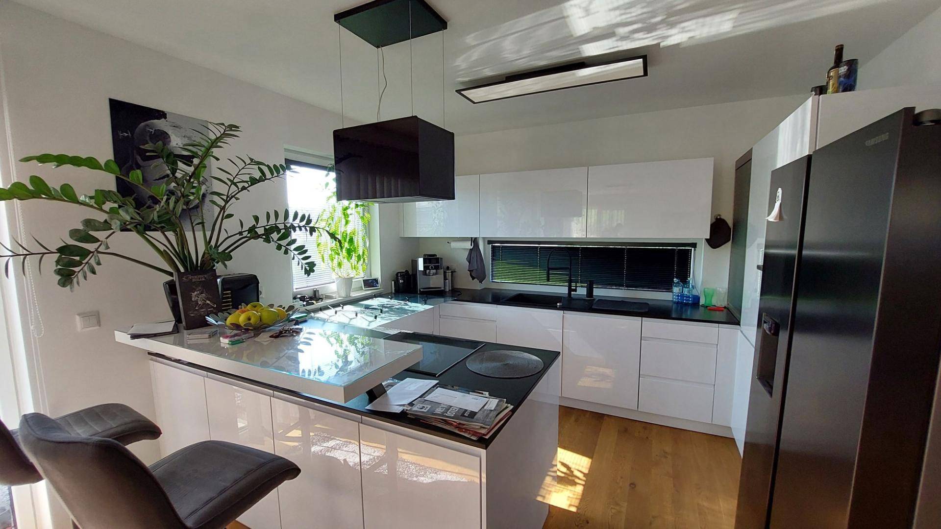 Moderne Küche mit weißen Hochglanzfronten, Kochinsel und schwarzen Arbeitsplatten.