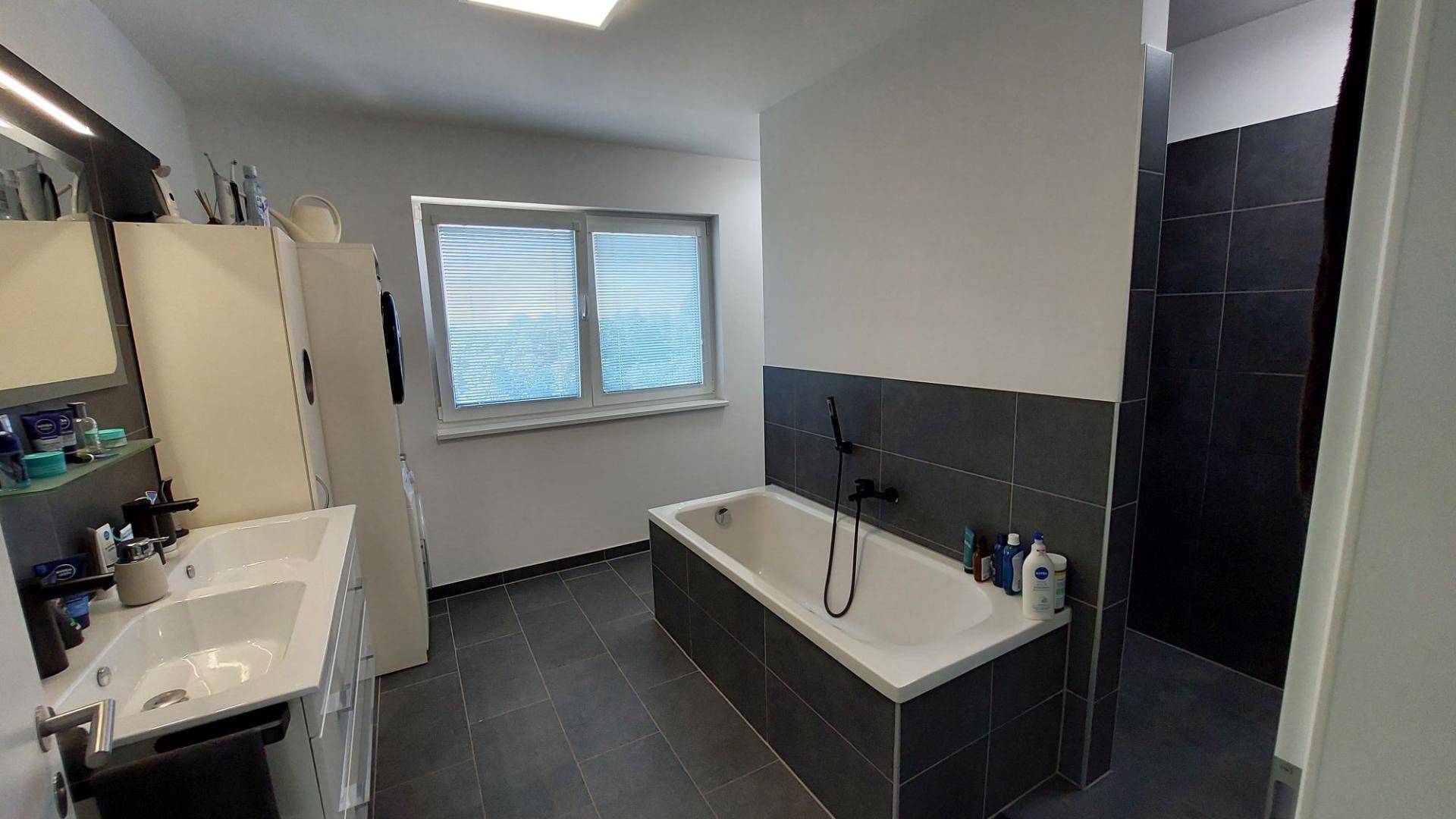 Modernes Badezimmer mit grauen Fliesen, Badewanne, begehbarer Dusche und Doppelwaschbecken.