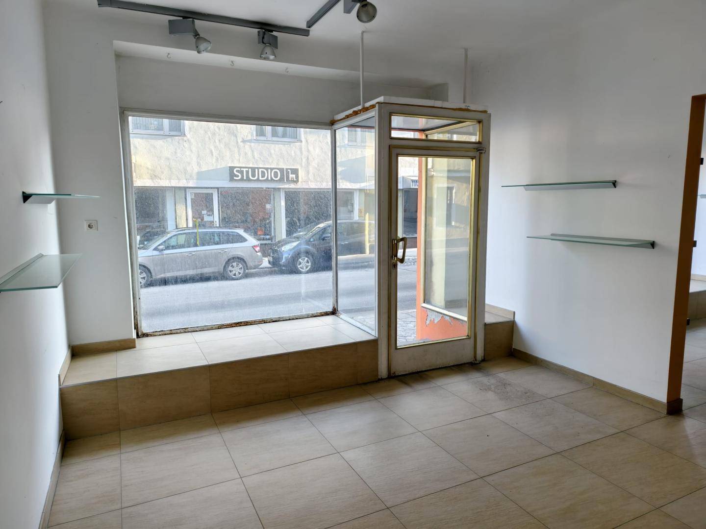 Geräumiger Innenraum mit großen Schaufenstern zur Straße und Glasregalen an den Wänden.