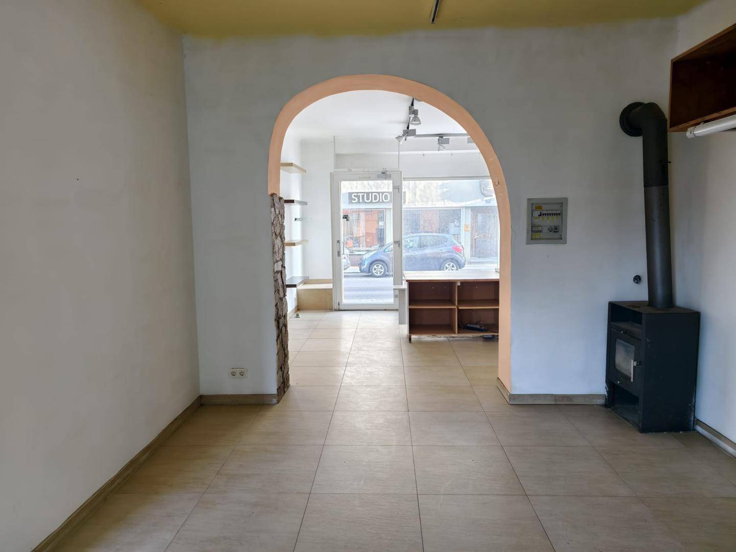 Innenraum mit einem Kaminofen und einem großen Bogen, der zu einem vorderen Bereich mit Schaufenster führt.