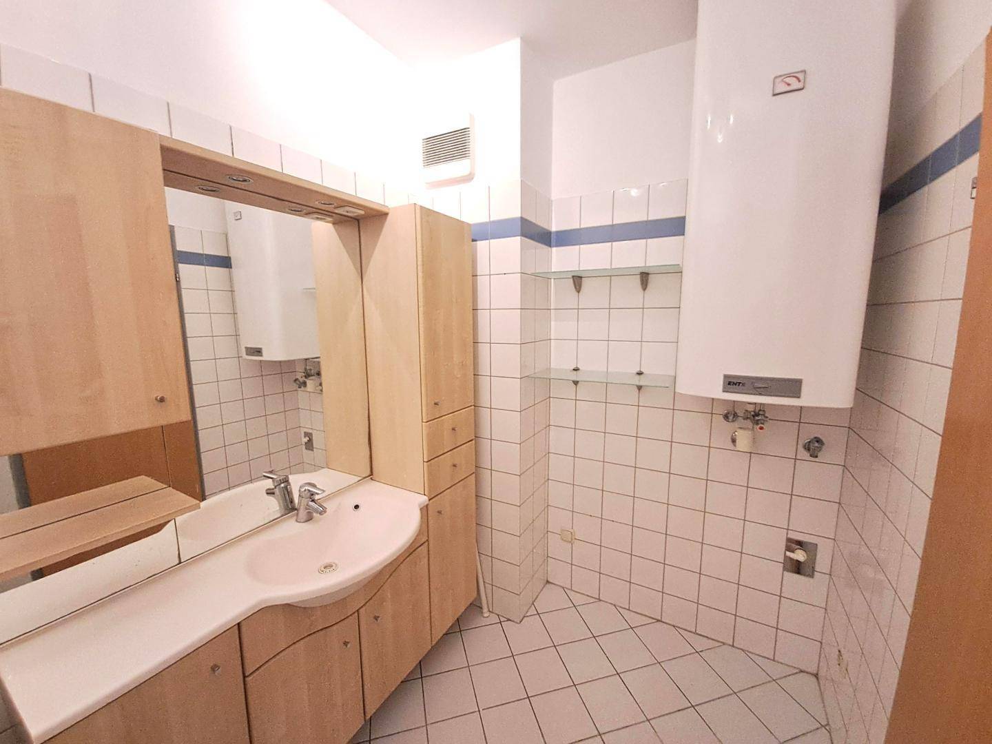 Badezimmer mit weißen Fliesen, Holzwaschtisch und einem Wandspiegel.