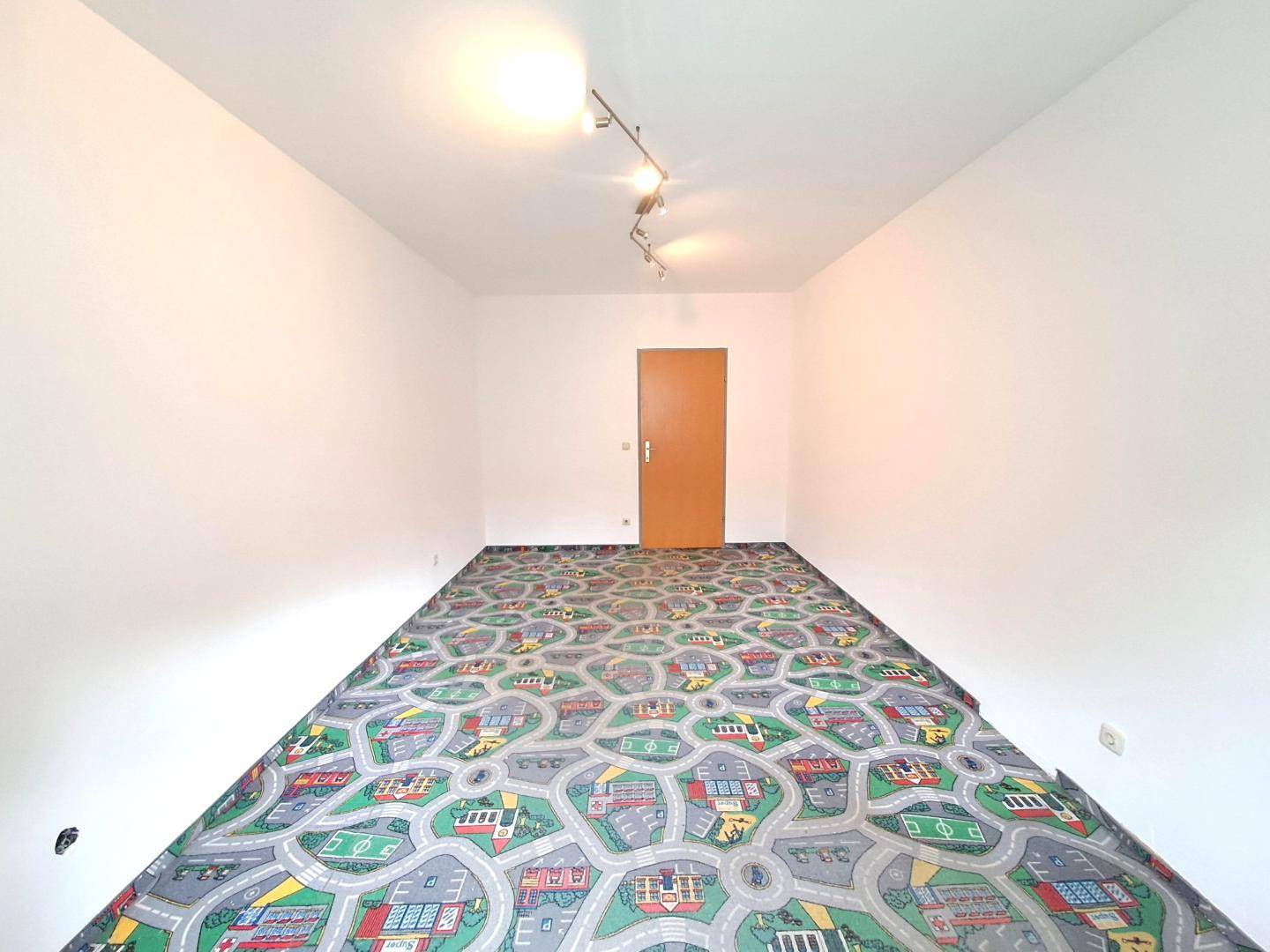 Helles Zimmer mit farbenfrohem Spielteppich und einer schlichten Holztür.