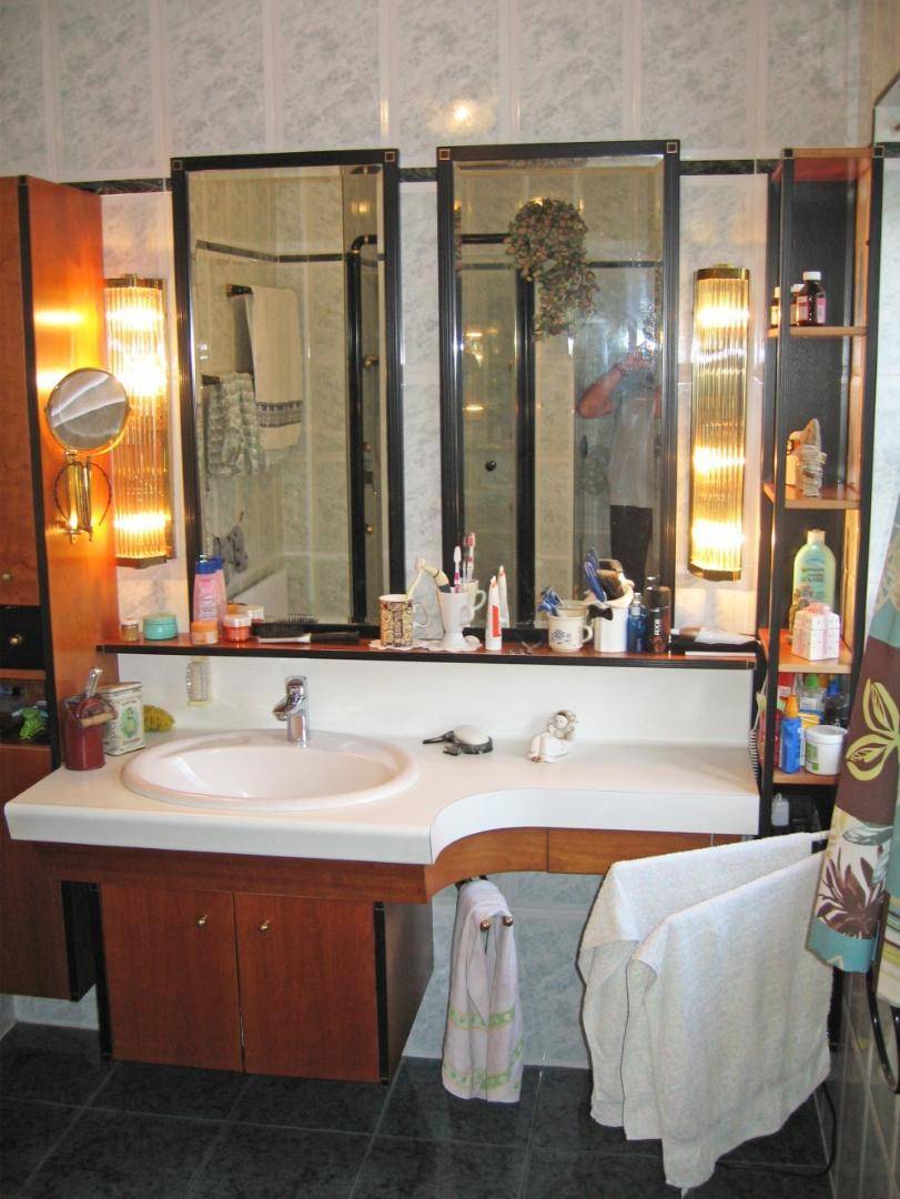 Badezimmer mit Einzelwaschbecken, großem Spiegelschrank und älteren, funktionalen Armaturen.