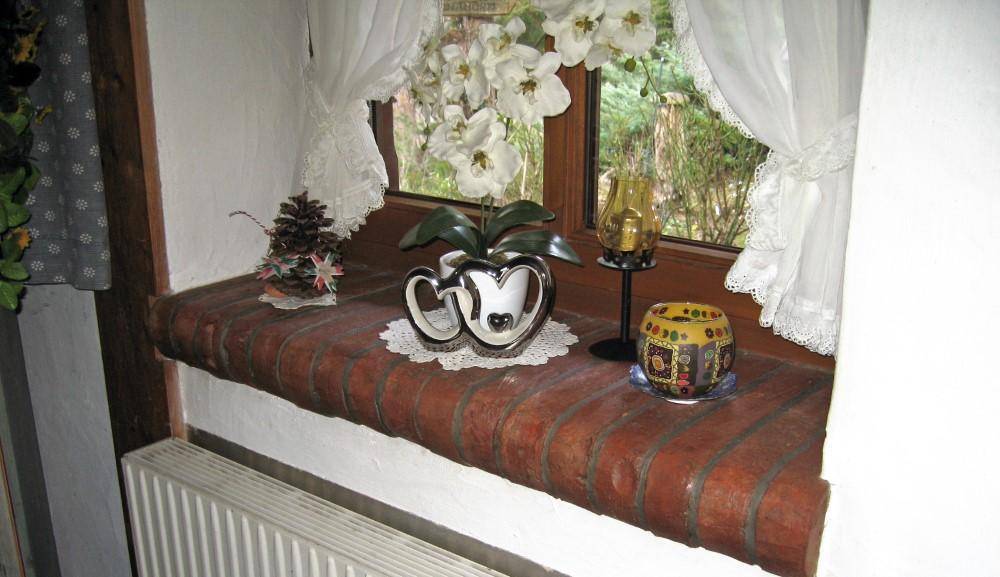 Detailansicht einer Fensterbank aus Ziegelstein mit traditionellen Dekorationen und Ausblick.