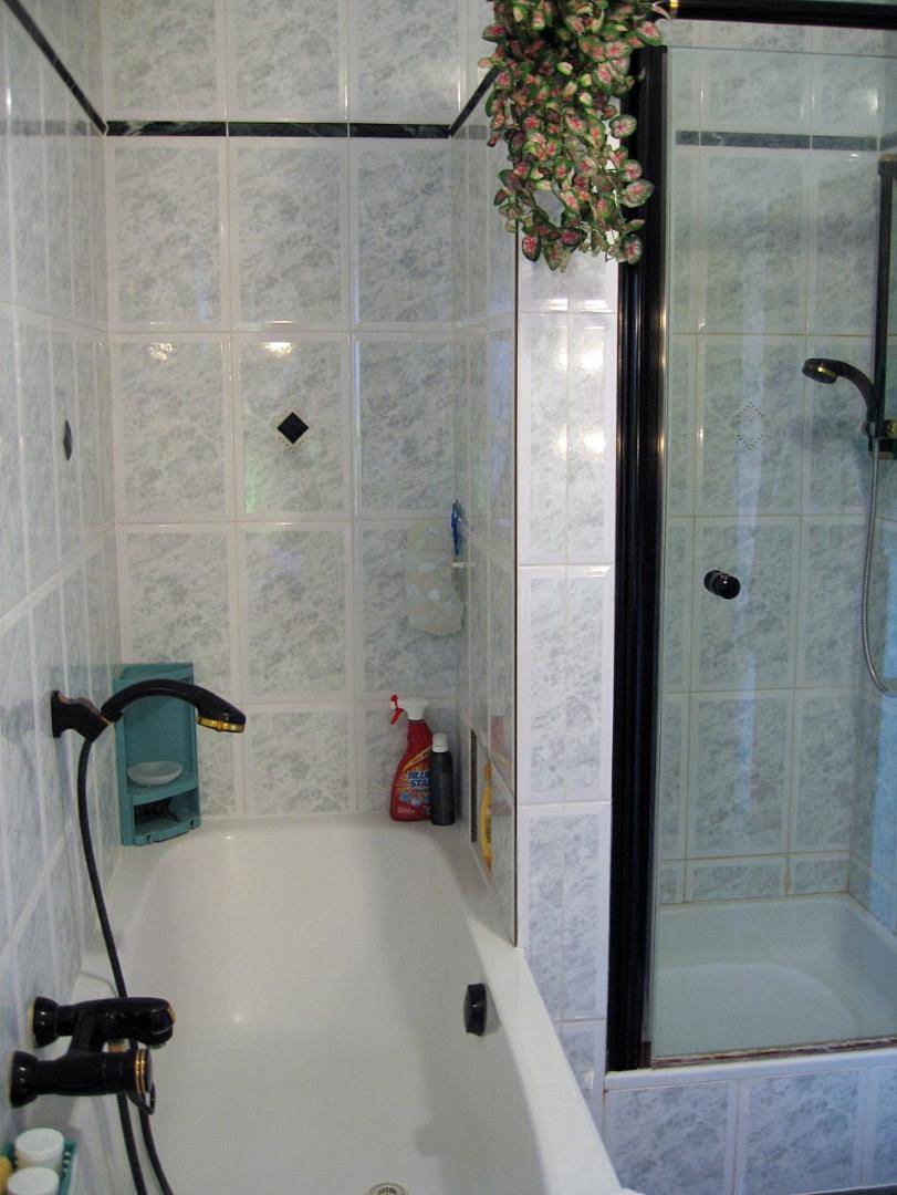 Badezimmer mit Badewanne und separater Duschkabine, gefliest in hellen Tönen und Schwarzakzenten.